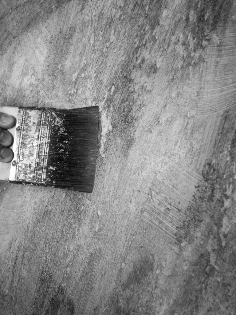zweiter Teil Bild Wandbemalung mit Pinsel Ein Pinsel streicht über eine strukturierte, graue Oberfläche.