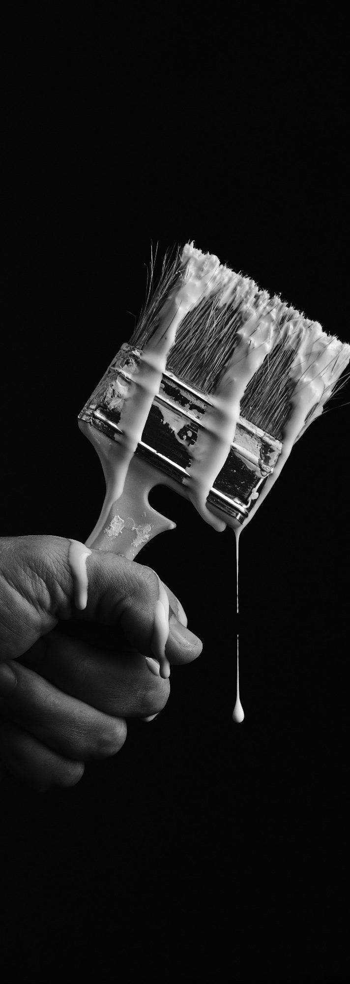 Handwerkszeug Eine Hand hält einen Pinsel mit tropfender Farbe vor schwarzem Hintergrund.